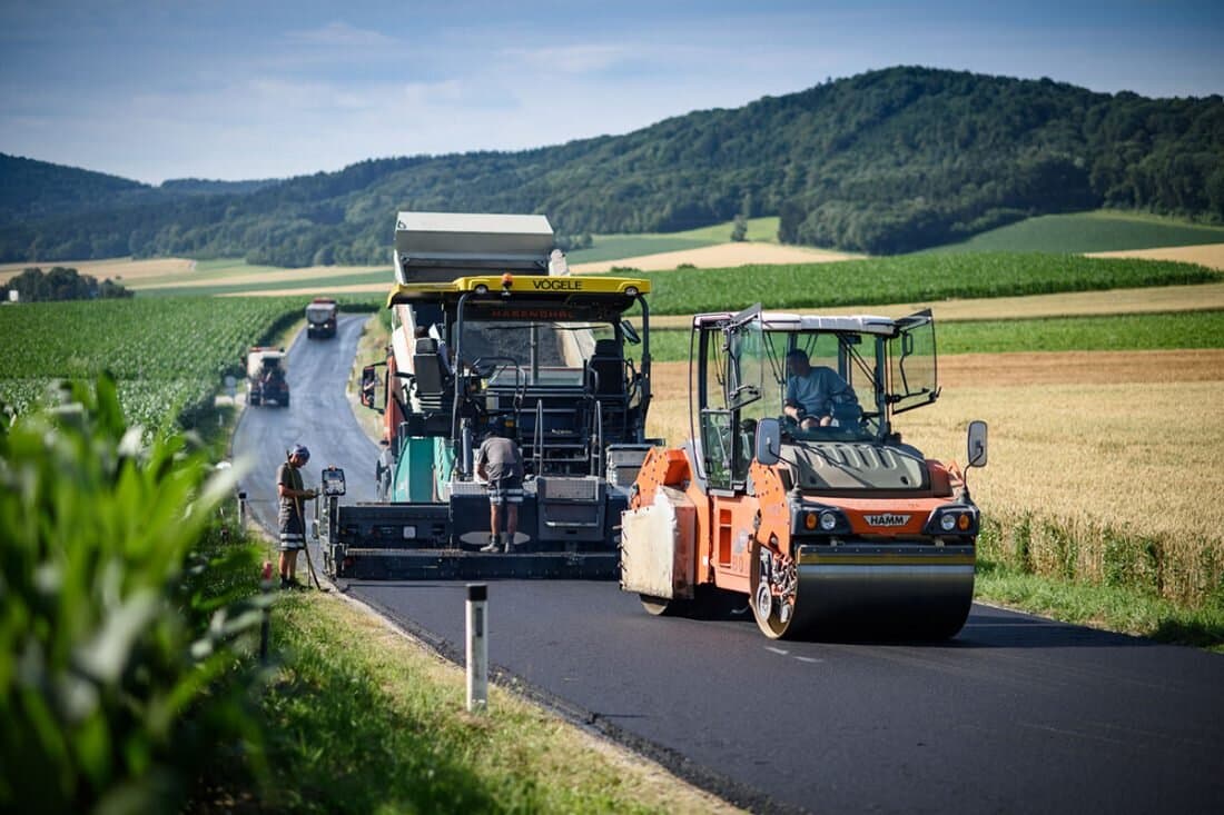 Straßenwalze auf frischem Asphalt vor Hügellandschaft