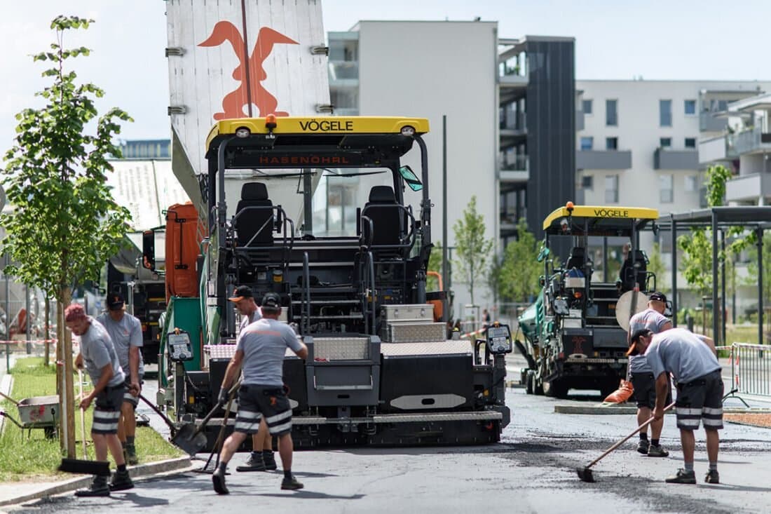 Asphaltfertiger mit Arbeitern im Siedlungsgebiet
